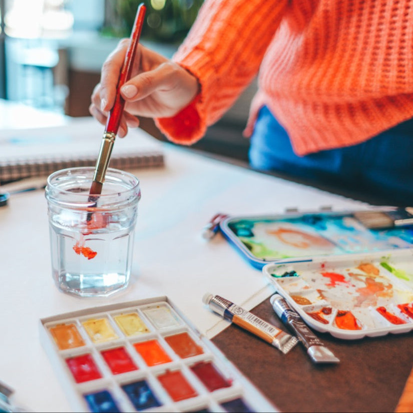 Person painting with watercolors on a table with art supplies